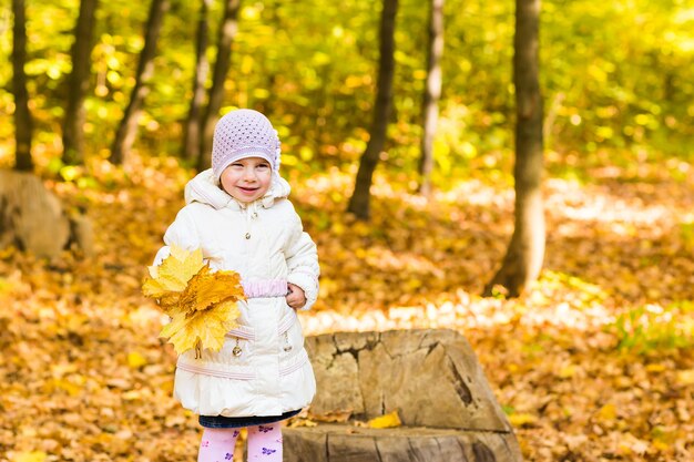 Portret szczęśliwa mała dziewczynka bawi się żółtymi jesiennymi liśćmi w naturalnym na zewnątrz