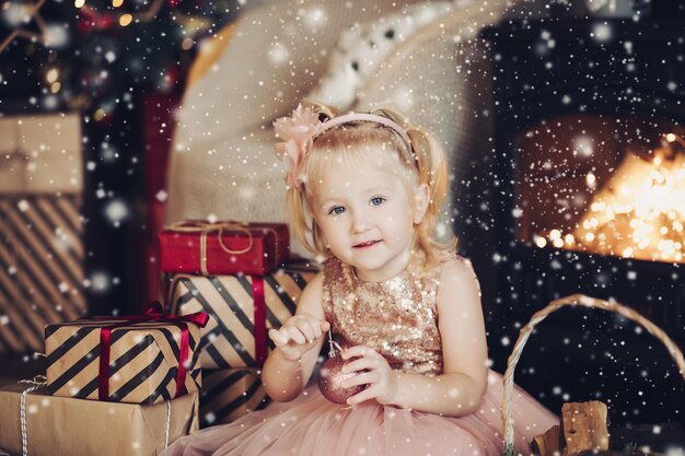 Portret szczęśliwa mała śliczna dziewczyna w olśniewającej świątecznej sukience pozuje przy bożym narodzeniem wnętrzem