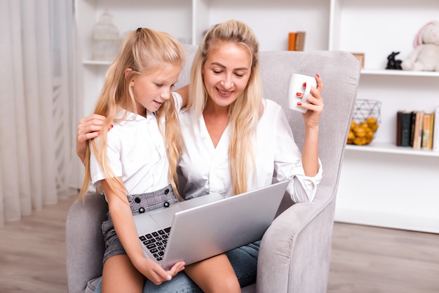 Zdjęcie portret szczęśliwa matka pracuje online z laptopem podczas gdy siedzący w domu z jej śliczną córką.