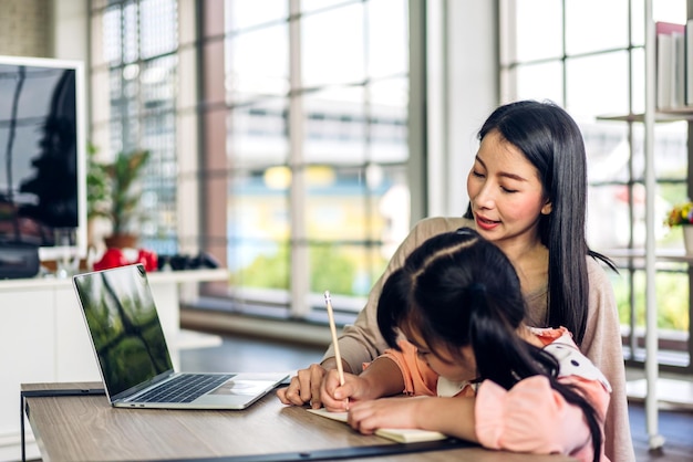 Portret szczęśliwa miłość azjatycka matka rodzinna uczy małą córkę azjatycka dziewczyna uczy się i studiuje na stoleMama i azjatycka młoda dziewczyna pisze z książką i ołówkiem robi pracę domową w szkole domowej w domuEdukacja