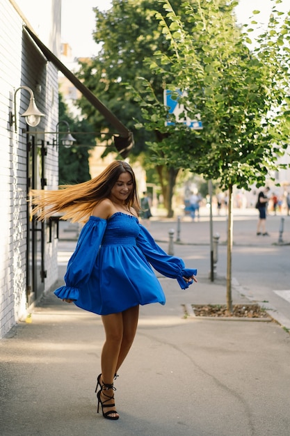 Portret szczęśliwa młoda kobieta ubrana w niebieską sukienkę śmiejąc się patrząc na kamerę stojącą na ulicy miejskie ba...