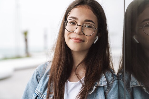 Portret szczęśliwa młoda ładna kobieta studentka w okularach spaceru na świeżym powietrzu, odpoczynek słuchania muzyki w słuchawkach.