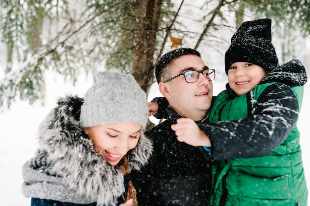 Portret szczęśliwa rodzina podmuchowy śnieg w winter park. Ojciec, matka i chłopiec dzieci bawią się i bawią na śnieżnym zimowym spacerze w przyrodzie.