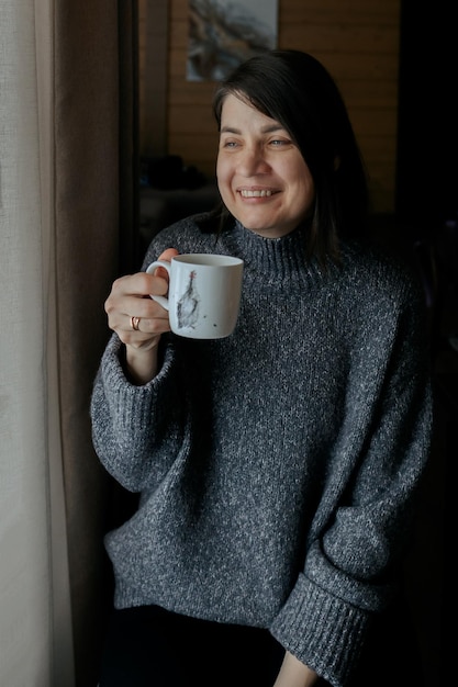 Portret szczęśliwa uśmiechnięta kobieta Dziewczyna z filiżanką kawy Kobieta pije herbatę w domu przez okno