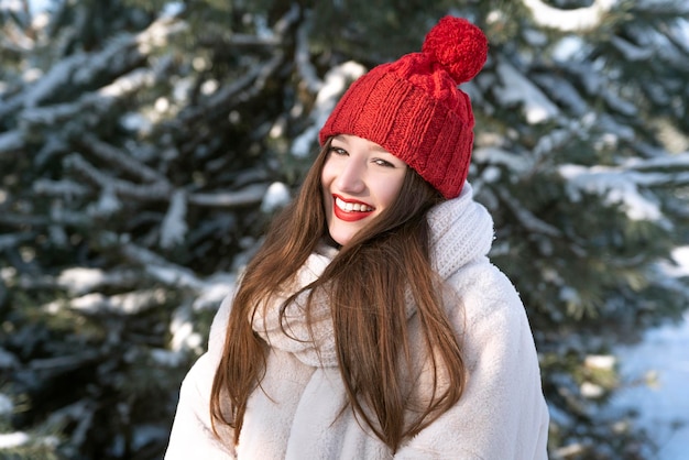 Portret szczęśliwa uśmiechnięta młoda brunetki kobieta w trykotowym czerwonym kapeluszu i mitynkach w zima parku Rozochocona dziewczyna