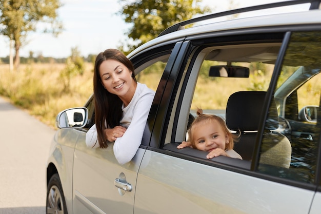 Portret szczęśliwa zachwycona kobieta o ciemnych włosach siedzi w samochodzie z córeczką na tylnym siedzeniu rodziny patrząc przez okno samochodu wyrażające pozytywne emocje