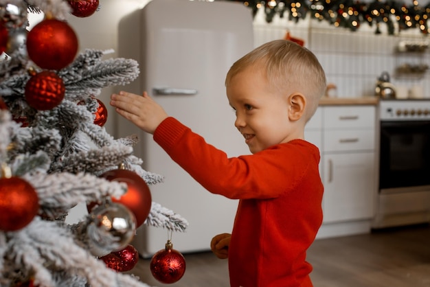 Portret szczęśliwego chłopca patrzącego na dekoracyjną zabawkową piłkę przy choince