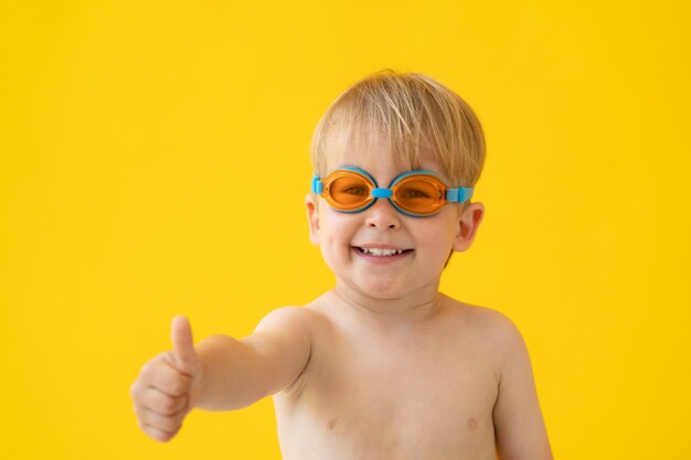 Portret szczęśliwego dziecka pokazuje kciuki do góry przeciw żółtej ścianie na wakacjach.