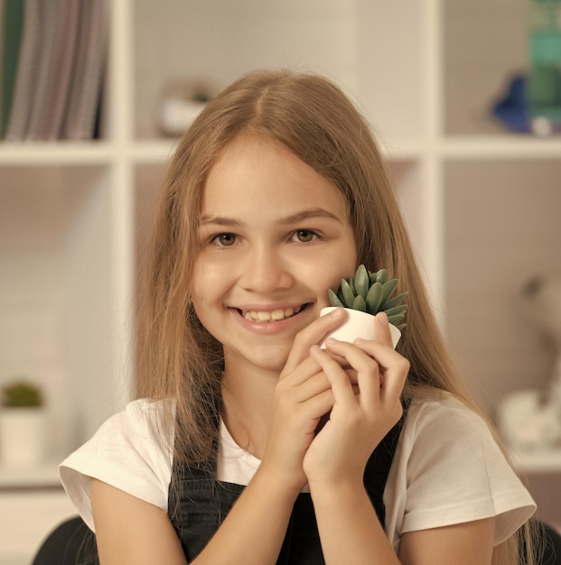 Portret szczęśliwego dziecka trzyma doniczkową roślinę w szkolnej klasie