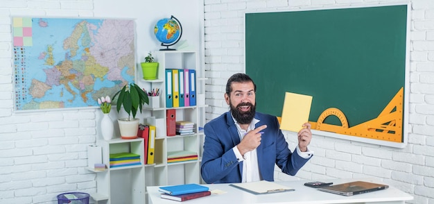 Portret szczęśliwego hipsterskiego faceta uśmiechającego się siedząc przy komputerze z laptopem do e-learningu i podręcznika do szkoły edukacji wiedzy