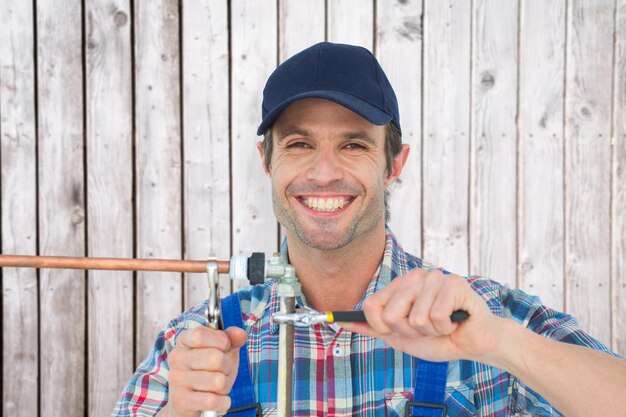 Portret szczęśliwego hydraulika ustalającego drymbę przed cyfrowo wytwarzanymi szarymi drewnianymi deskami