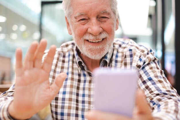 Portret szczęśliwego kaukaskiego starszego mężczyzny rozmawiającego przez telefon komórkowy podczas rozmowy wideo przystojnego brodatego starszego mężczyzny siedzącego za pomocą smartfona