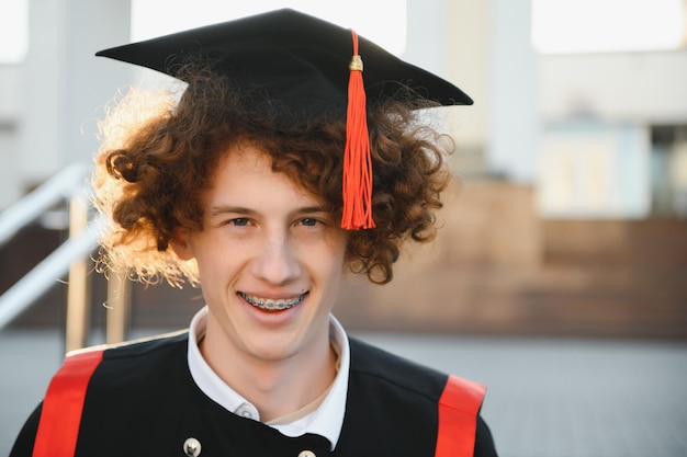 Portret szczęśliwego kaukaskiego studenta w sukni i kapeluszu, który ukończył szkołę średnią, patrząc na uśmiechniętą kamerę