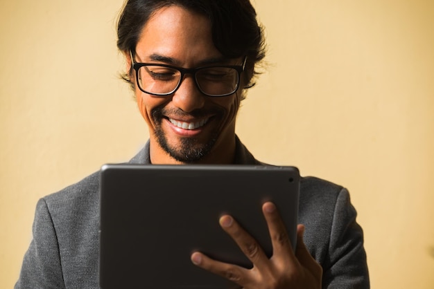 Zdjęcie portret szczęśliwego latynosa używającego swojego tabletu na żółtym tle