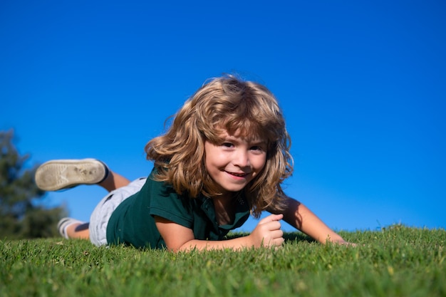 Portret szczęśliwego małego chłopca leżącego na trawie w parku Plenerowy portret ładnego małego chłopca