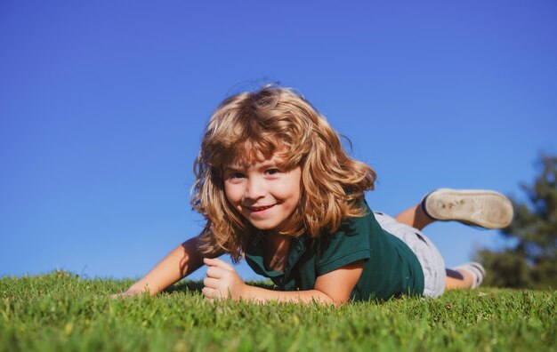Portret szczęśliwego małego chłopca leżącego na trawie w parku Plenerowy portret ładnego małego chłopca