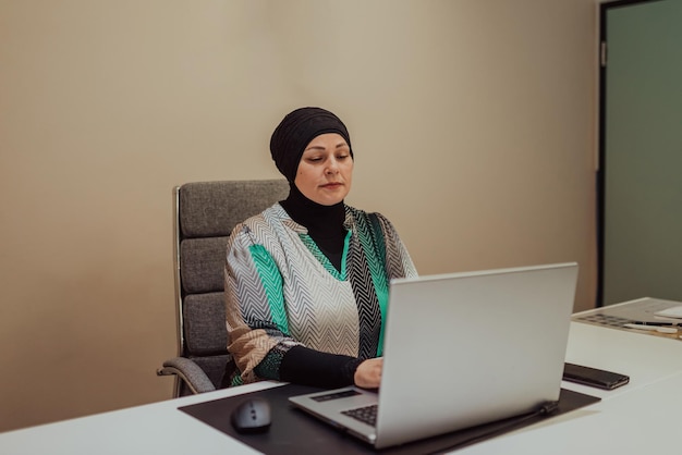 Portret szczęśliwego menedżera muzułmańskiego hidżabu w jasnym biurze Uśmiecha się do kamery siedząc przy biurkuWysokiej jakości zdjęcie
