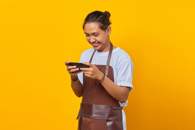 Portret Szczęśliwego Młodego Azjatyckiego Baristy Grającego W Grę Wideo Na Telefonie Komórkowym Na żółtym Tle