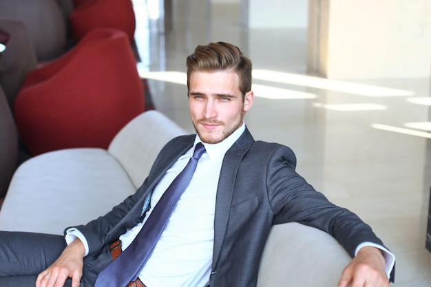 Portret szczęśliwego młodego biznesmena siedzącego na kanapie w holu hotelu