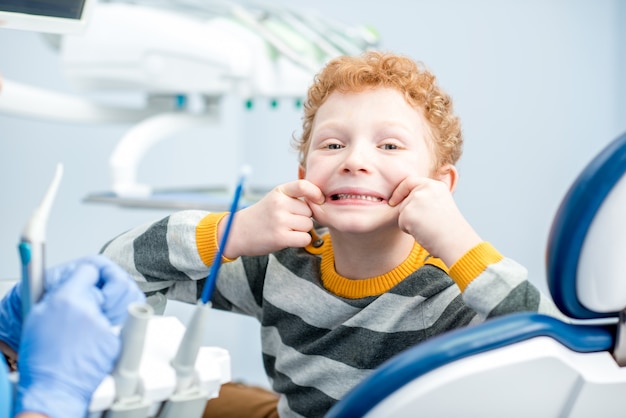 Portret szczęśliwego młodego chłopca z uśmiechem zębów, siedzącego na fotelu dentystycznym w gabinecie stomatologicznym