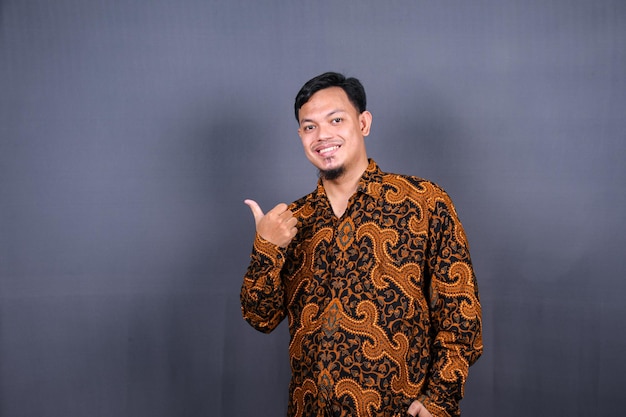 Portret szczęśliwego młodego człowieka w batiku w indonezji, wskazując palcem od miejsca kopiowania. odosobniony