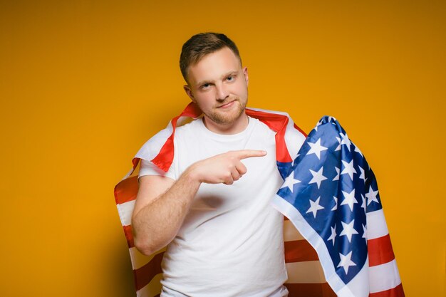 Portret szczęśliwego młodego mężczyzny z brodą w zwykłych ubraniach, trzymającego flagę USA na żółto
