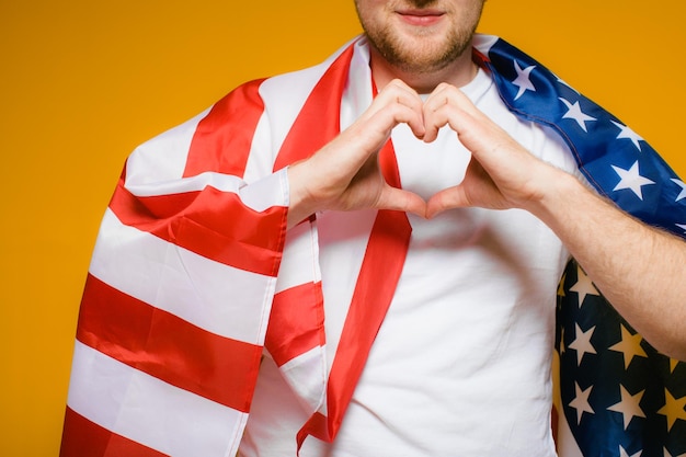 Portret szczęśliwego młodego mężczyzny z brodą w zwykłych ubraniach, trzymającego flagę USA na żółto