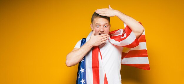 Portret szczęśliwego młodego mężczyzny z brodą w zwykłych ubraniach, trzymającego flagę usa