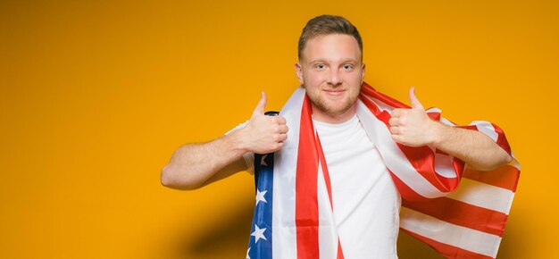 Portret szczęśliwego młodego mężczyzny z brodą w zwykłych ubraniach, trzymającego flagę usa