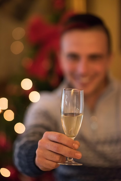 Portret szczęśliwego młodzieńca z lampką szampana świętującego ferie zimowe w domu pięknie udekorowane na święta