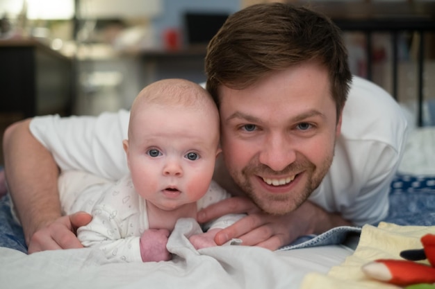 Zdjęcie portret szczęśliwego ojca i jego uroczej małej córeczki leżących razem na łóżku, patrzących na kamerę