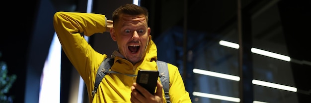 Portret szczęśliwego, podekscytowanego mężczyzny patrzącego z szczęściem na ekran smartfona.
