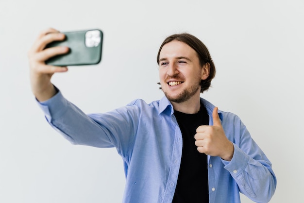 Portret Szczęśliwego Przypadkowego Mężczyzny Biorącego Selfie I Pokazującego Kciuk W Górę Gest Na Białym Tle