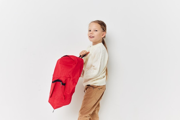 Portret szczęśliwego uśmiechniętego dziecka dziewczyna czerwony plecak stylowe ubrania jasne tło