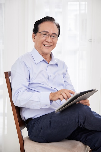 Portret szczęśliwego uśmiechniętego starszego biznesmena siedzącego na krześle i korzystającego z aplikacji na cyfrowym tablecie