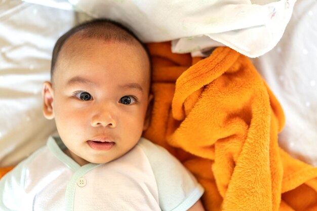 Zdjęcie portret szczęśliwego uśmiechu azjatyckiego chłopca relaksującego patrzącego na kamerę śliczny azjatycki noworodek na łóżku w domu