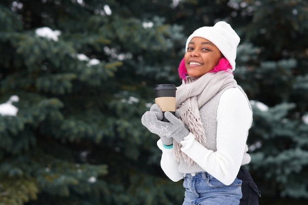 Portret szczęśliwej afroamerykańskiej młodej kobiety w zimowy śnieżny dzień w uśmiechu parku śnieżnego, pij kawę