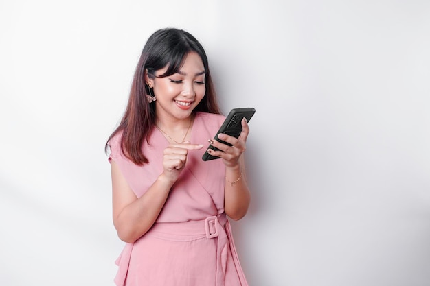 Portret szczęśliwej azjatyckiej kobiety ubranej na różowo i trzymającej telefon odizolowany białym tłem