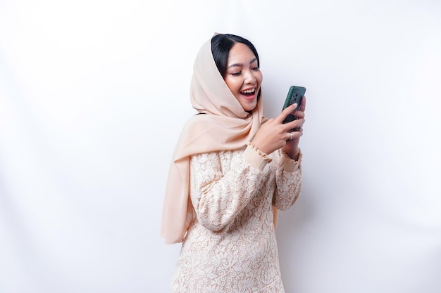 Portret szczęśliwej azjatyckiej muzułmanki w hidżabie trzymającej telefon odizolowany białym tłem