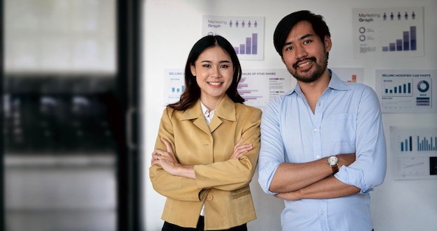 Portret szczęśliwej azjatyckiej pary biznesowej pozuje z rękami skrzyżowanymi stojąc w nowoczesnym biurze
