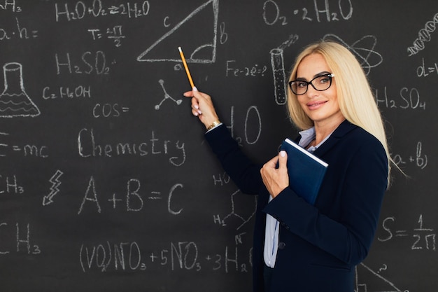 Portret szczęśliwej blondynki nauczycielki kobiety stojącej w pobliżu tablicy w klasie
