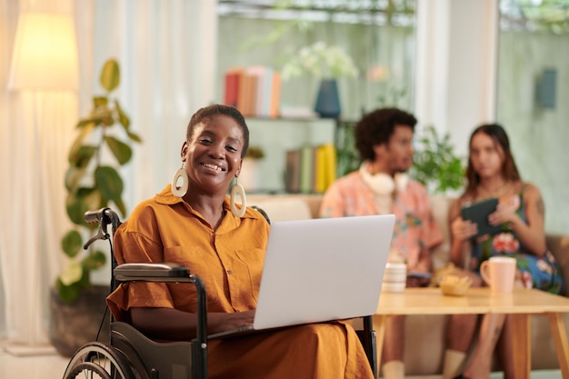 Portret szczęśliwej czarnej kobiety z niepełnosprawnością pracującej na laptopie w salonie dla studentów
