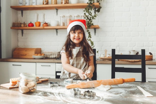 Portret Szczęśliwej Dziewczynki W Czapce Mikołaja Rozwałkującej Ciasto Na Kuchennym Stole Dziecko Przygotowujące świąteczne Ciasteczka