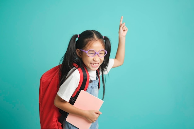 Portret szczęśliwej dziewczynki w plecaku wskazującej palcem z udanym pomysłem