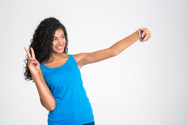 Portret szczęśliwej kobiety afro american robi selfie zdjęcie na białym tle na białej ścianie