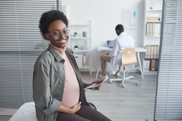 Portret szczęśliwej kobiety w ciąży uśmiecha się do kamery siedząc w klinice