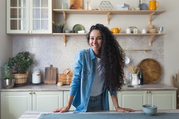 Portret szczęśliwej latynoskiej kobiety w domu w kuchni kobieta z kręconymi włosami uśmiechnięta i patrząca