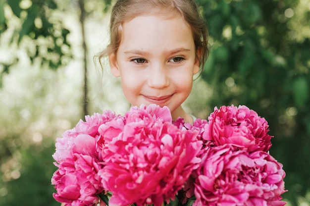 portret szczęśliwej małej siedmioletniej dziewczynki rasy kaukaskiej, trzymającej w rękach bukiet różowej piwonii