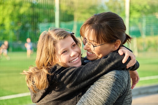 Portret szczęśliwej matki i córki w wieku przed nastoletnim przytulającej się na świeżym powietrzu w pobliżu stadionu sportowego pola piłkarskiego Rodzina szczęście wolny czas styl życia związek miłość Dzień Matki koncepcja macierzyństwa