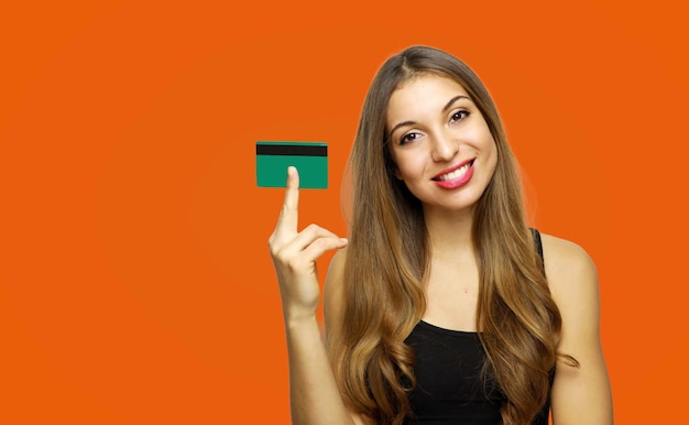 Portret szczęśliwej młodej kobiety trzymającej kartę kredytową na pomarańczowym tle